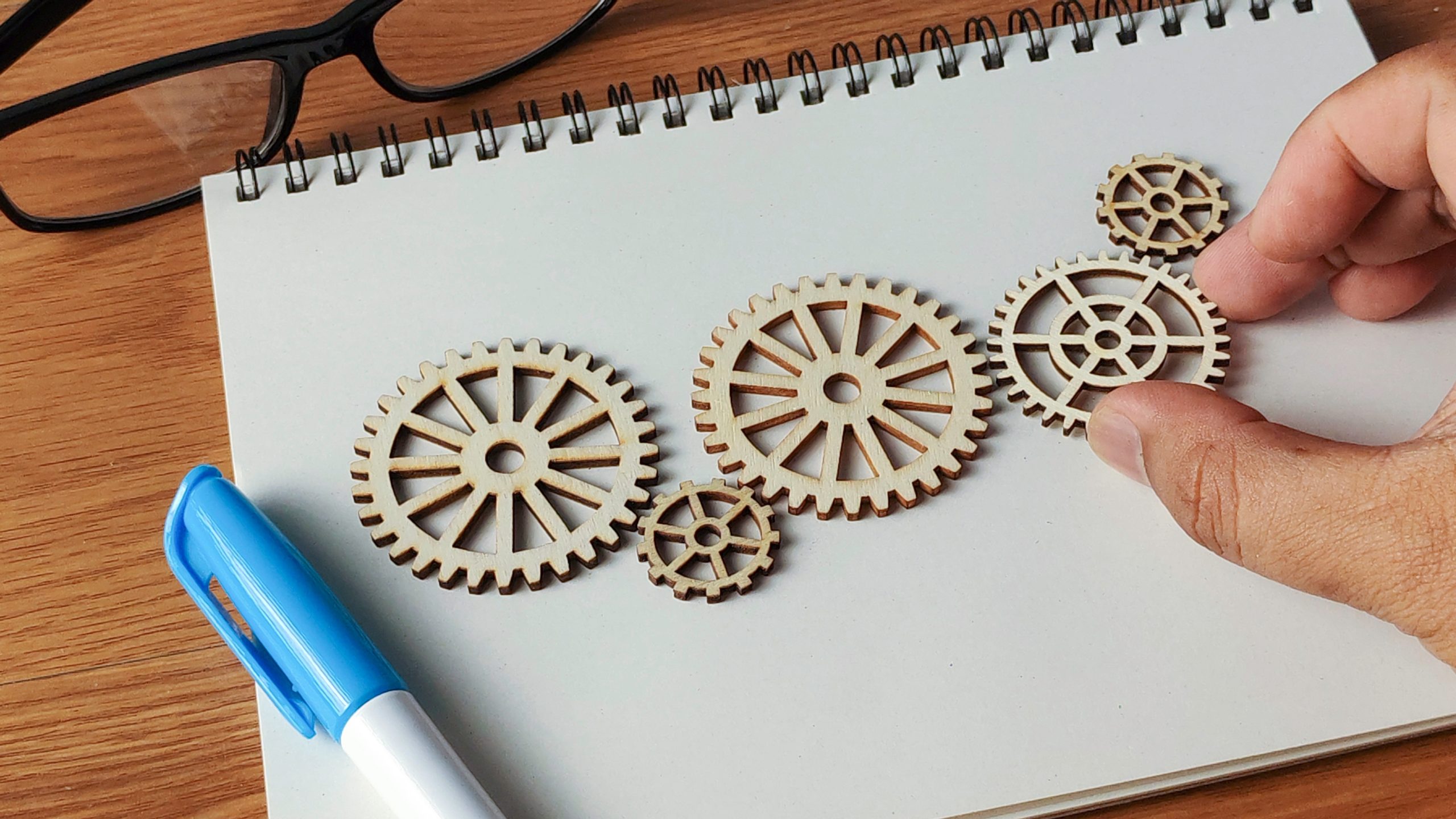 Hand,Arranging,Wooden,Cogwheels,On,A,Notebook:,Conceptualizing,Innovation,,Problem About us